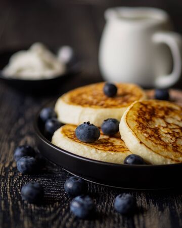 Pancakes (cheese cakes, cottage cheese) with blueberries on a dark wooden tableの写真素材