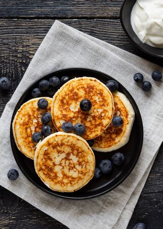 Pancakes (cheese cakes, cottage cheese) with blueberries on a dark wooden tableの写真素材
