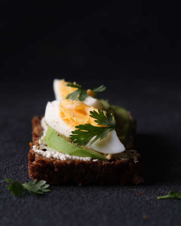 Rye bread appetizer with curd cheese, egg and avocado on black background. Vertical photo.の写真素材