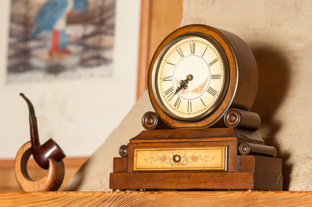 Vintage wooden clock and a tobacco pipe on a stand on the mantelpiece  in high quality の写真素材