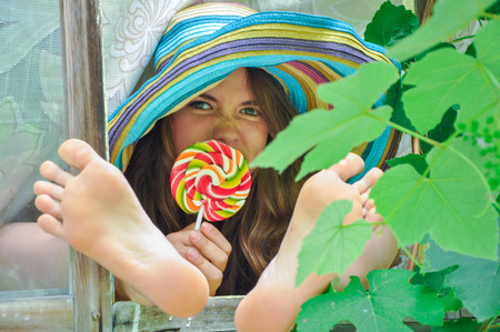 funny girl wearing a colorful hat with lollipop in a window with grape leaves in high qualityの写真素材