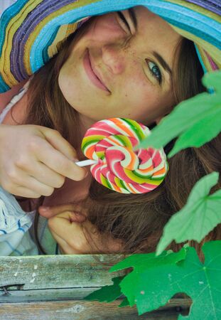 funny girl wearing a colorful hat with lollipop in a window with grape leaves in high qualityの写真素材
