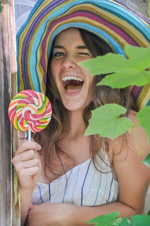 funny girl wearing a colorful hat with lollipop in a window with grape leaves in high qualityの写真素材