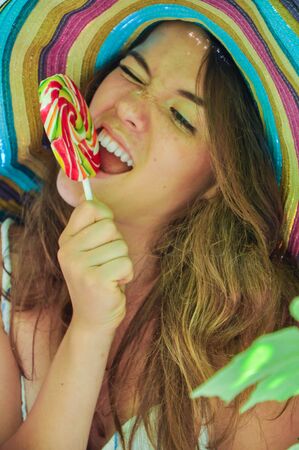 funny girl wearing a colorful hat with lollipop in a window with grape leaves in high qualityの写真素材