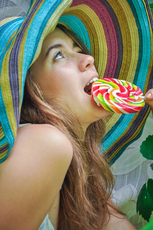 funny girl wearing a colorful hat with lollipop in a window with grape leaves in high qualityの写真素材