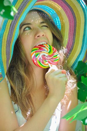 funny girl wearing a colorful hat with lollipop in a window with grape leaves in high qualityの写真素材