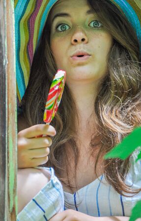 funny girl wearing a colorful hat with lollipop in a window with grape leaves in high qualityの写真素材