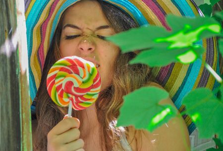 funny girl wearing a colorful hat with lollipop in a window with grape leaves in high qualityの写真素材