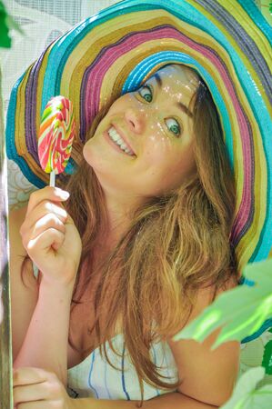 funny girl wearing a colorful hat with lollipop in a window with grape leaves in high qualityの写真素材