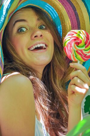 funny girl wearing a colorful hat with lollipop in a window with grape leaves in high qualityの写真素材