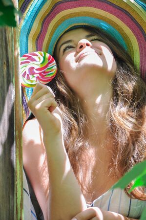 funny girl wearing a colorful hat with lollipop in a window with grape leaves in high qualityの写真素材