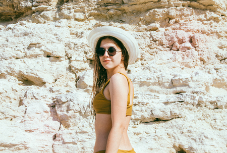 Beautiful girl in a bikini, hat and sunglasses sunbathing on the background of white rocksの写真素材