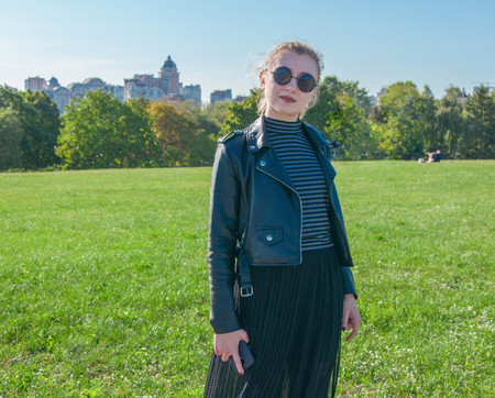 A beautiful blonde girl stands and smiles on the green lawn backgroundの写真素材