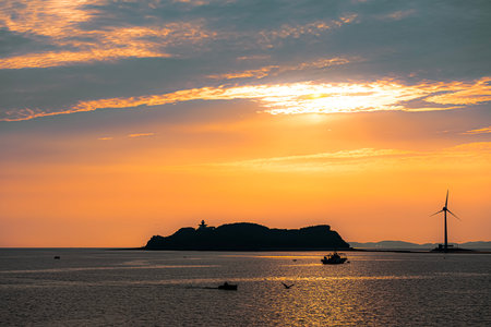 Beautiful sunset over the sea with silhouette of a lighthouse and boatsの写真素材