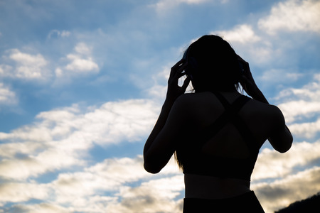 Beautiful young sportswoman in sportswear and earphones listening to music resting after workout session on sunset.の写真素材