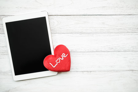 Red heart and White digital tablet on blackwooden tableの写真素材