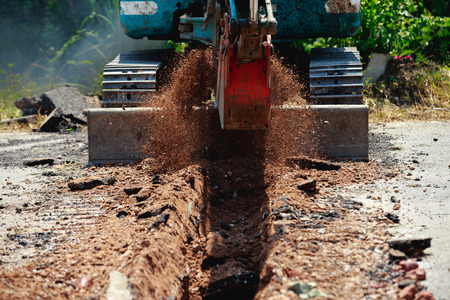Backhoe is digging road to lay water pipe.の写真素材