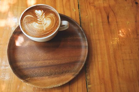 A cup of hot latte art in wooden tray on wooden table with the lightの写真素材