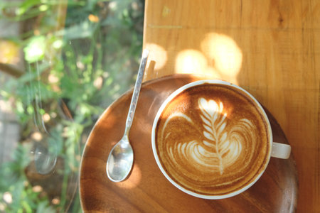 A cup of hot latte art in wooden tray on wooden table with the light and spoon