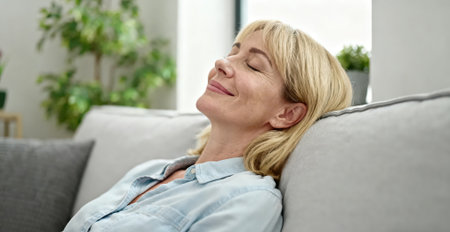 Relaxed mature woman with closed eyes lying on sofa at homeの素材