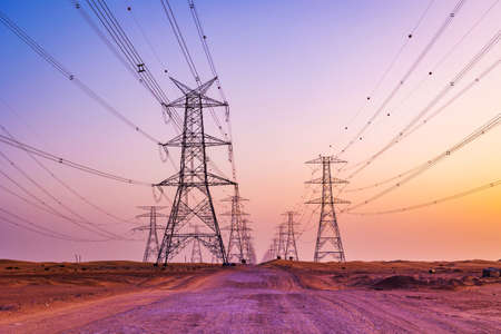 High voltage tower with electricity transmission power lines against the colorful sky, low angle view. Dubai Al Qudra Desert United Arab Emirates.の写真素材