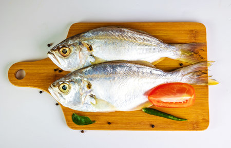 Fresh raw Fish garnished with Black Pepper, Chilly, Curry Leaves and Tomato placed on a wooden...