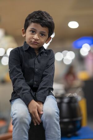 Cute Little Indian boy sitting at table and playing in restaurantの写真素材