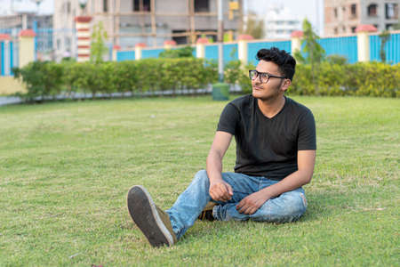 Fashion portrait of Indian Guy wearing a black t-shirt sits on the groundの写真素材