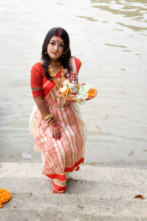 Portrait of beautiful Indian Bengali female model in ethnic saree and jewellery holding plate of...