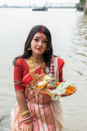 Portrait of beautiful Indian Bengali female model in ethnic saree and jewellery holding plate of religious offeringの写真素材