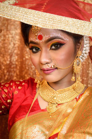 Stunning Indian bride dressed in traditional wedding clothes sari embroidered with gold jewellery and a veil smiles tender in studio lighting indoorの写真素材