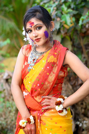 Portrait of pretty young indian girl wearing traditional saree and jewellery, playing with colors on...