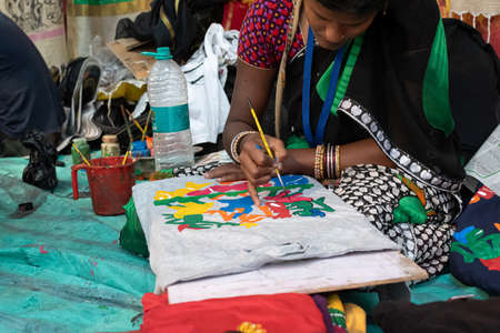 An Indian Unidentified middle-aged woman paints on colourful handicraft items for sale in Kolkata in handicrafts trade fair. It is rural Industry in West Bengal, India on December 2019のeditorial素材