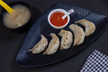 Picture of steamed chicken stuffed momo served in a black plate along with chicken soup in a bowl...
