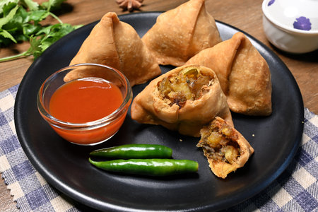 Picture of samosa or singara, a crispy and spicy triangle shape snack with a savoury filling of mashed potato, peas, and spices served in a black plate with green chili pepper and chutney.の写真素材