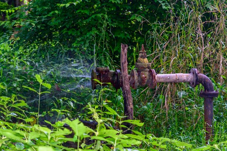 Old iron Metallic water pipe leaking. Rusty burst pipe spraying water.の写真素材