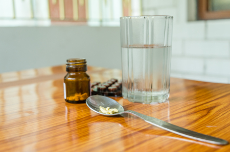View of antioxidants vitamin tablet, pill blisters, a bottle of drug, capsule in measuring spoon, with glass of water placed on the table. Medical Pharmacy theme. Side view, Close up with copy space.の写真素材