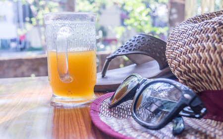 Modern women essential accessories for sunday weekend activities on wooden table. Sunglasses placed over Straw hat, flip flops, with a glass of lime juice with natural sunlight coming from window.の写真素材