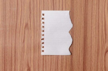 Sheet of notebook paper with torn edge blank ripped piece on isolated over wooden table background....