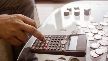 Cropped Image Of Businessman counting coins Using Calculator at Desk In Office. Businessperson Hand Counting Coins. Business Finance Savings and Investment concept. Conceptual Save money for future.の写真素材