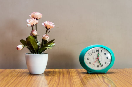 A flower vase and an alarm clock on table isolated from background. Design element. Copy space room...