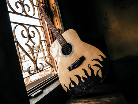 An acoustic guitar placed next to the old vintage window with soft sunlight coming from. Nostalgia guitar chords. Summer melody background. Close up.の写真素材