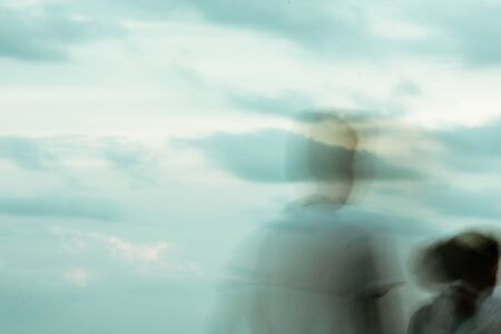 Shadow faces of people man and woman in front. Abstract motion blur background against of beautiful sunset sky with soft clouds and silhouettes. Summer season. Copy space room for text on left side.の写真素材