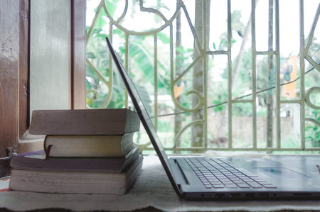 Heap of books and a laptop on window sunlight in morning. A daily routine during social distancing period. Stay home, Work from home, Remote Work and Business Continuity background.の写真素材