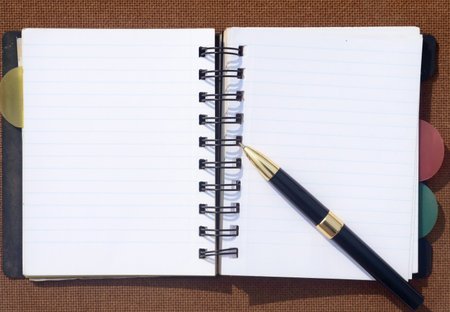 A pen placed over open notebook on Brown Color Hard cork board.. High angel view. Business Education...