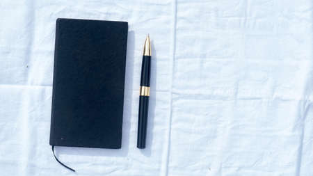 A notebook and a pen on white cotton cloth. High angel view. Business Education background. Copy space room for text on right side.の写真素材