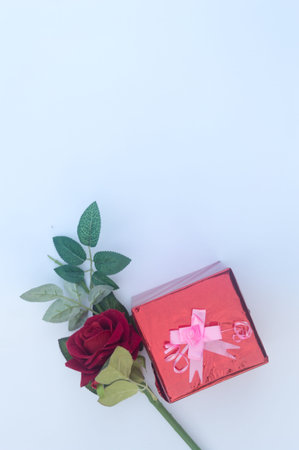 Gift box wrapped and tied with ribbon and a red rose in white background. Table top view. Flat Lay. Copy Space. Vertical.の写真素材