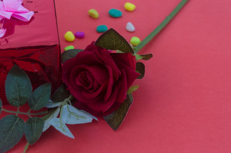 Close up red rose placed on a table near gift box with tied bow ribbon in red background. High angle view. Design for valentine's day, anniversary or holiday celebration decoration.の写真素材