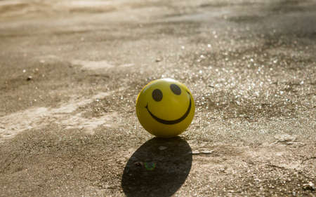 The iconic yellow smiley face with its perfect circle, two oval eyes and a large semi-circular mouth representing a symbol of happiness isolated on sand and shadow background. Happy smile backgrounds.の写真素材