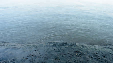 Muddy river banks in low tide next to wave water. Alluvial soils deposited by the river. Nature background. Close up.の写真素材